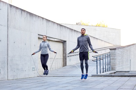 fitness, sport, people, exercising and lifestyle concept - man and woman skipping with jump rope...
