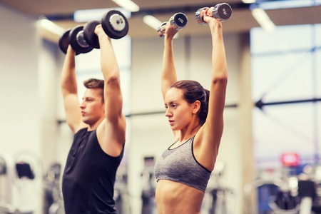 sport, fitness, lifestyle and people concept - smiling man and woman with dumbbells flexing muscles in gymの写真素材