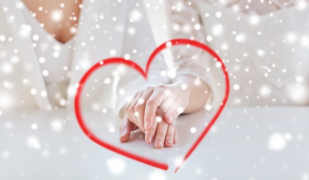 people, homosexuality, same-sex marriage and love concept - close up of happy married lesbian couple hands over snow effectの写真素材