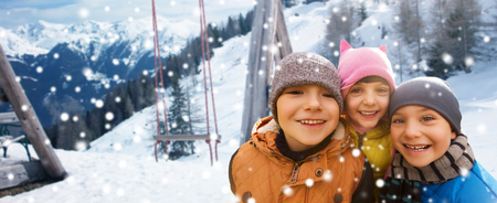 childhood, friendship, winter holidays, vacation and people concept - group of happy kids hugging over swing and snowy mountains backgroundの写真素材