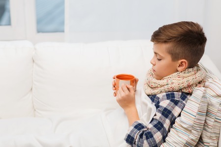 childhood, healthcare, people and medicine concept - ill boy with flu lying in bed and drinking tea at homeの写真素材