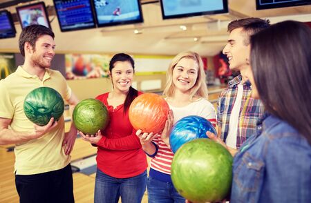 people, leisure, sport, friendship and entertainment concept - happy friends holding balls and talking in bowling clubの写真素材