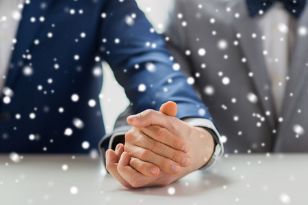 people, homosexuality, same-sex marriage and love concept - close up of happy male gay couple holding hands on wedding over snow effectの写真素材