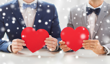 people, homosexuality, same-sex marriage, valentines day and love concept - close up of happy married male gay couple holding red paper heart shapes on wedding over snow effectの写真素材