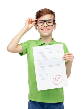 childhood, school, education and people concept - happy smiling boy in eyeglasses holding paper with test resultの写真素材