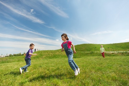 summer, childhood, leisure and people concept - group of happy kids playing tag game and running on green field outdoorsの写真素材