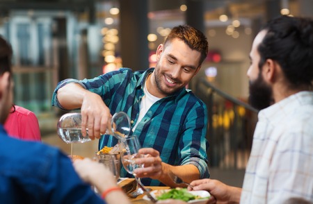 leisure, people and holidays concept - smiling man with friends pouring water from jug at restaurant leisure, people and holidays concept - smiling man with friends pouring water from jug at restaurant