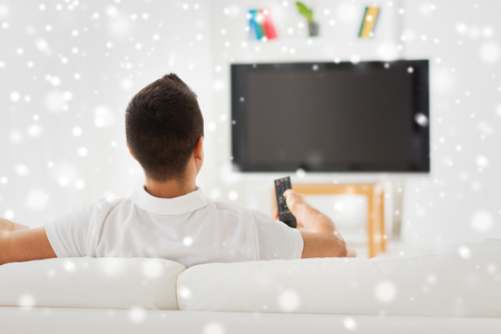 leisure, technology, mass media and people concept - man watching tv and changing channels at home from back over snow effectの写真素材