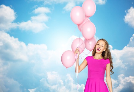 summer, people, holidays, birthday and fashion concept - happy young woman or teen girl in pink dress with helium air balloons over blue sky and clouds backgroundの写真素材