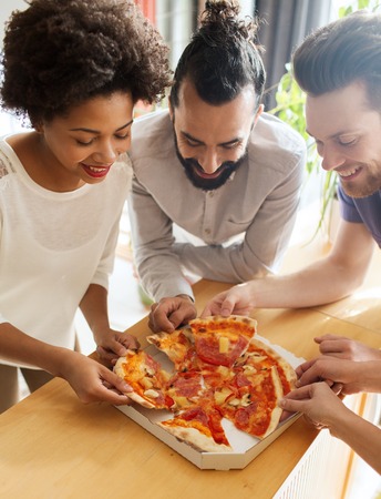 business, food, lunch and people concept - happy business team eating pizza in officeの写真素材