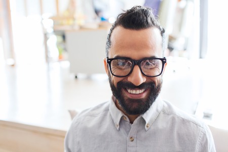 business, startup, and people concept - happy smiling latin man with eyeglasses and beard at officeの写真素材