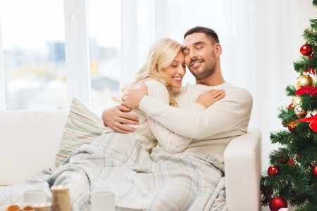 family, christmas, holidays, love and people concept - happy couple covered with plaid sitting on sofa at homeの写真素材