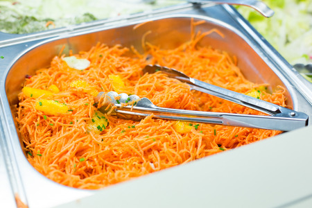 food, catering, eating and cooking concept - close up of spicy korean carrot salad with tongs in metallic containerの写真素材