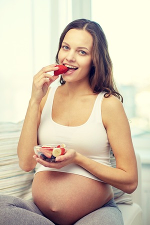 happy pregnant woman eating fruits at home