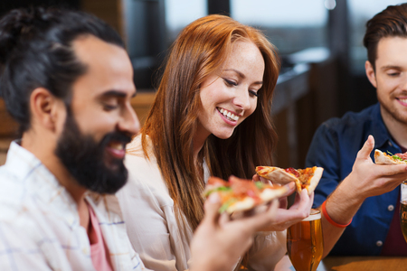 smiling friends eating pizza and drinking beer at restaurant or pub