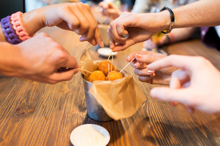 fast food, junk food, unhealthy eating and culinary concept - close up of people hands taking cheese balls with skewers at bar or restaurantの写真素材
