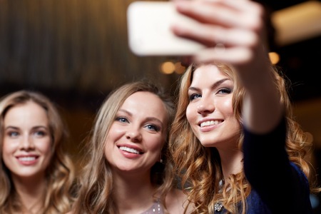 celebration, friends, bachelorette party, technology and holidays concept - happy women with smartphone taking selfie at night clubの写真素材