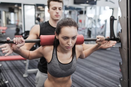 sport, fitness, teamwork, weightlifting and people concept - young woman and personal trainer with barbell flexing muscles in gymの写真素材