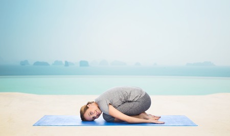 fitness, sport, people and healthy lifestyle concept - happy woman making yoga in child pose on mat over infinity edge pool at hotel resort backgroundの写真素材