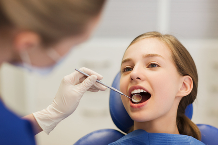 people, medicine, stomatology and health care concept - happy female dentist with mirror checking patient girl teeth up at dental clinic officeの写真素材