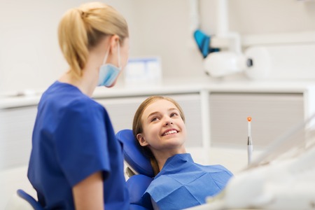 people, medicine, stomatology and health care concept - happy female dentist with patient girl talking at dental clinic officeの写真素材