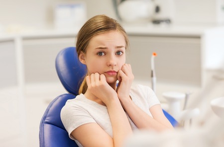 people, medicine, stomatology and phobia concept - scared and terrified patient girl at dental...