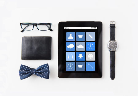 technology and objects concept - tablet pc computer with application icons, wallet, eyeglasses, bowtie and wristwatch on tableの写真素材