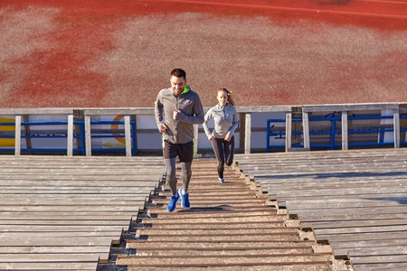 fitness, sport, exercising and lifestyle concept - happy couple running upstairs on stadiumの写真素材