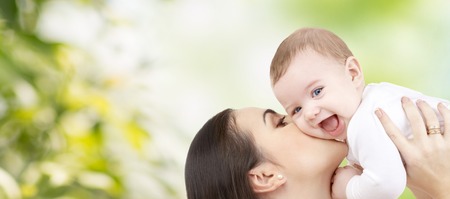 family, motherhood, children, parenthood and people concept - happy mother kissing her baby over green natural backgroundの写真素材