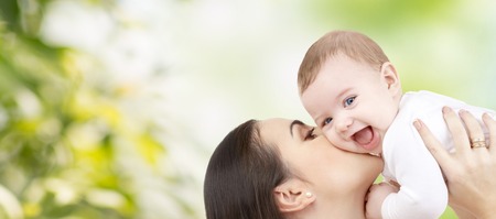 family, motherhood, children, parenthood and people concept - happy mother kissing her baby over green natural background