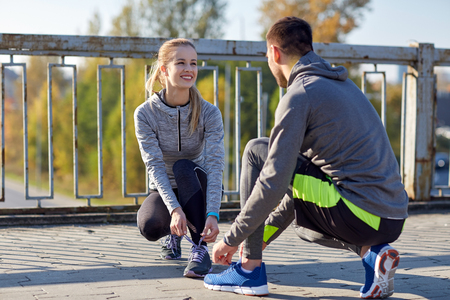 fitness, sport, people and lifestyle concept - smiling couple tying shoelaces outdoorsの写真素材