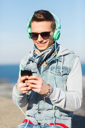 technology, lifestyle and people concept - smiling young man or teenage boy in headphones with smartphone listening to music outdoorsの写真素材