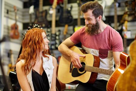 music, sale, people, musical instruments and entertainment concept - happy couple of musicians with guitar at music storeの写真素材