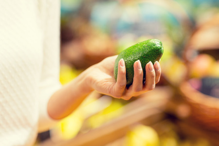 sale, shopping, food, consumerism and people concept - close up of woman hand holding avocado in marketの写真素材