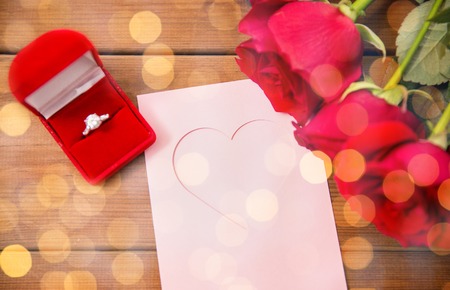 love, proposal, valentines day and holidays concept - close up of gift box with diamond engagement ring, red roses and greeting card on woodの写真素材