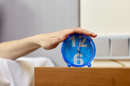 morning, awakening and people concept - close up of female hand on alarm clock in bedroomの写真素材