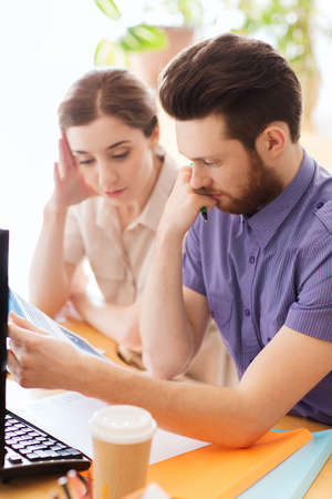 business, startup and people concept - creative team of man and woman with computer and files solving problem in officeの写真素材