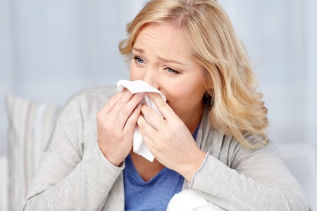health care, flu, hygiene and people concept - ill woman blowing nose to paper napkinの写真素材