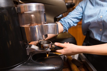 equipment, coffee shop, people and technology concept - close up of woman making coffee by machine at cafe bar or restaurant kitchenの写真素材