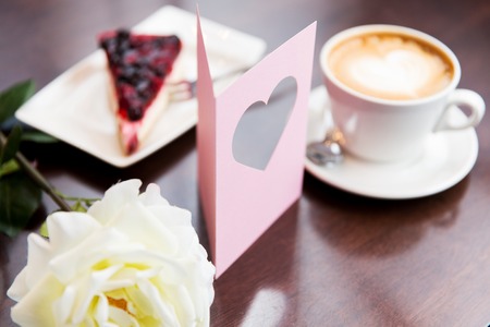 holidays, valentines day and love concept - close up of greeting card with heart, flower, cake and coffeeの写真素材