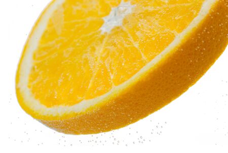 fruits, food and healthy eating concept - close up of slice of fresh orange falling or dipping in water with splash over white backgroundの写真素材