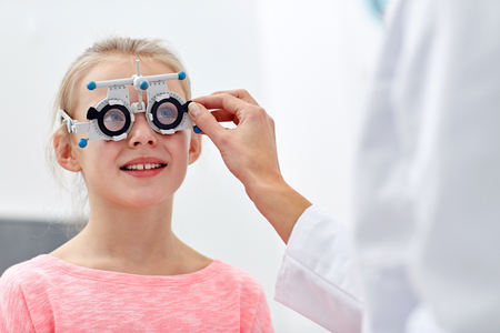 health care, medicine, people, eyesight and technology concept - optometrist with trial frame checking girl patient vision at eye clinic or optics storeの写真素材
