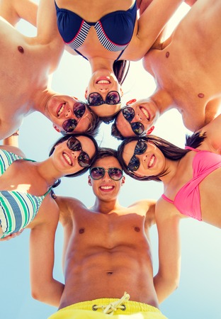 friendship, happiness, summer vacation, holidays and people concept - group of smiling friends wearing swimwear standing in circle over blue skyの写真素材