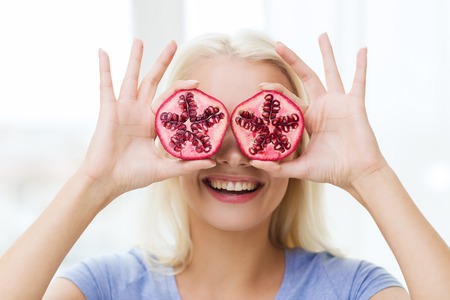 healthy eating, organic food, fruit diet, comic and people concept - happy woman having fun and covering her eyes with pomegranateの写真素材