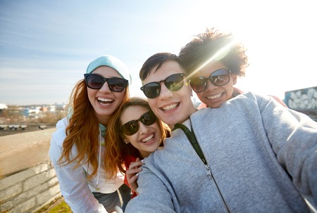 tourism, travel, people, leisure and technology concept - group of smiling teenage friends taking selfie on city streetの写真素材