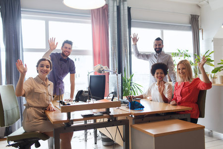 business, startup and office concept - happy creative team waving hands in officeの写真素材