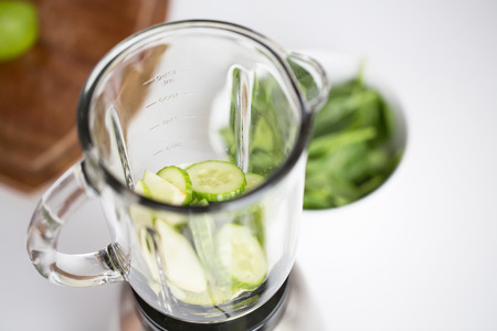 healthy eating, cooking, vegetarian food, detox and diet concept - close up of blender jar and green vegetables on table at homeの写真素材