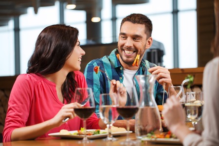leisure, people, eating and holidays concept - happy couple with friends having dinner at restaurantの写真素材