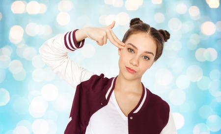 people, emotion, expression, stress and teens concept - bored teenage girl making headshot by finger...