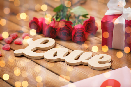 romance, valentines day and holidays concept - close up of word love, gift box, red roses and greeting card with heart-shaped candies on wood over lights backgroundの写真素材